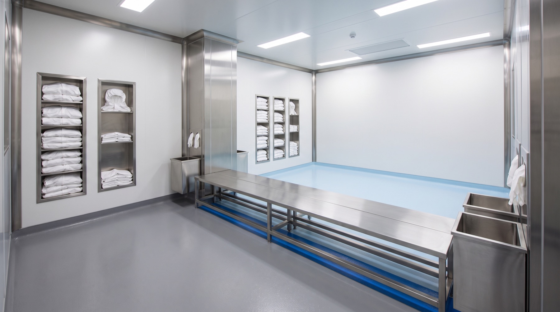 A gowning area with a stainless bench dividing the room, coverall and hood dispensers on the wall, glove and overshoe stations, and a step-over line marked on the floor